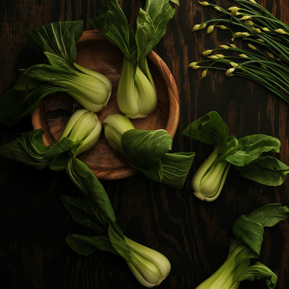 Several heads of fresh bok choy arranged on a dark wooden surface