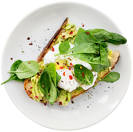 A slice of toasted bread topped with mashed avocado, a perfectly poached egg, fresh spinach leaves, and red pepper flakes on a white plate